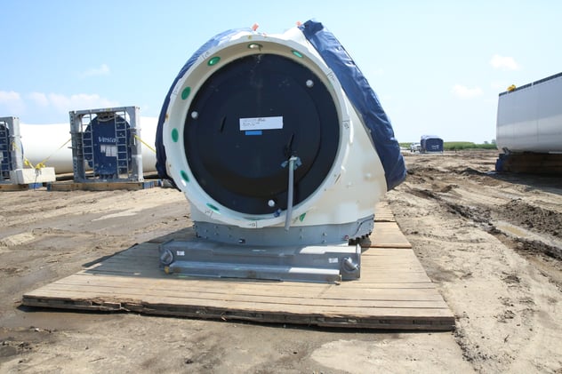 Wind turbine blade delivery across a stabilized access road constructed with matting solutions, enabling safe transport through agricultural terrain for renewable energy infrastructure projects.